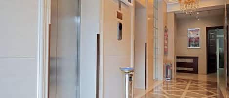 Un vestíbulo de hotel con mostrador de recepción, un panel informativo digital, un bote de basura y un suelo estampado.