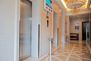 Un vestíbulo de hotel con mostrador de recepción, un panel informativo digital, un bote de basura y un suelo estampado.