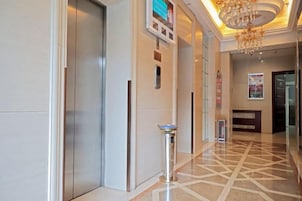 Un vestíbulo de hotel con mostrador de recepción, un panel informativo digital, un bote de basura y un suelo estampado.