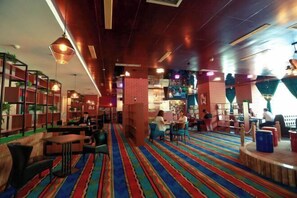 A restaurant with striped carpet, wooden tables, and chairs. There are shelves with plants and a brick wall in the background. - Tianlong Hotel (Baotou)