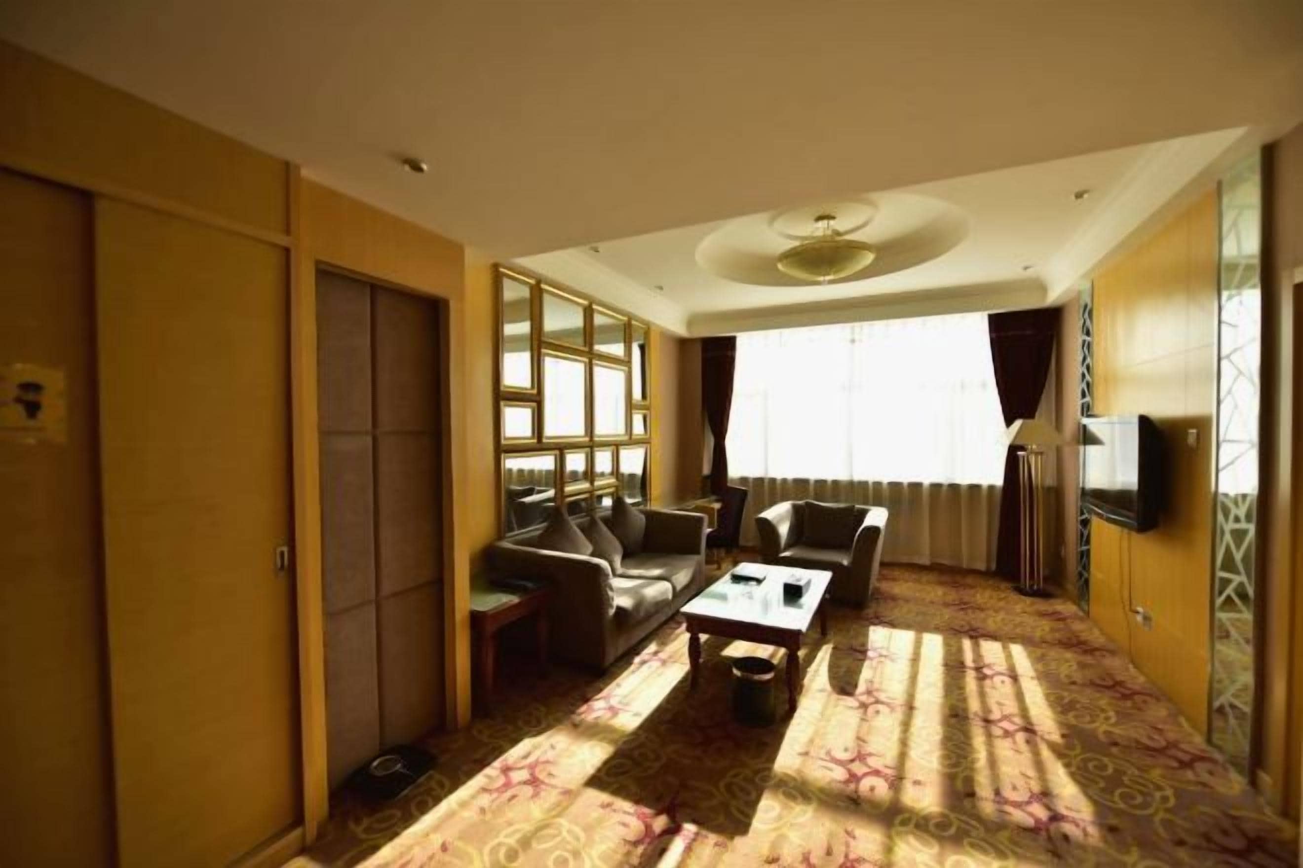 A hotel room with a sofa set, a coffee table, a TV, and a patterned carpet.
