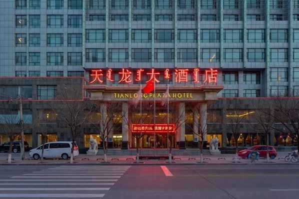 A hotel entrance with a large sign, a crosswalk, and a few vehicles.