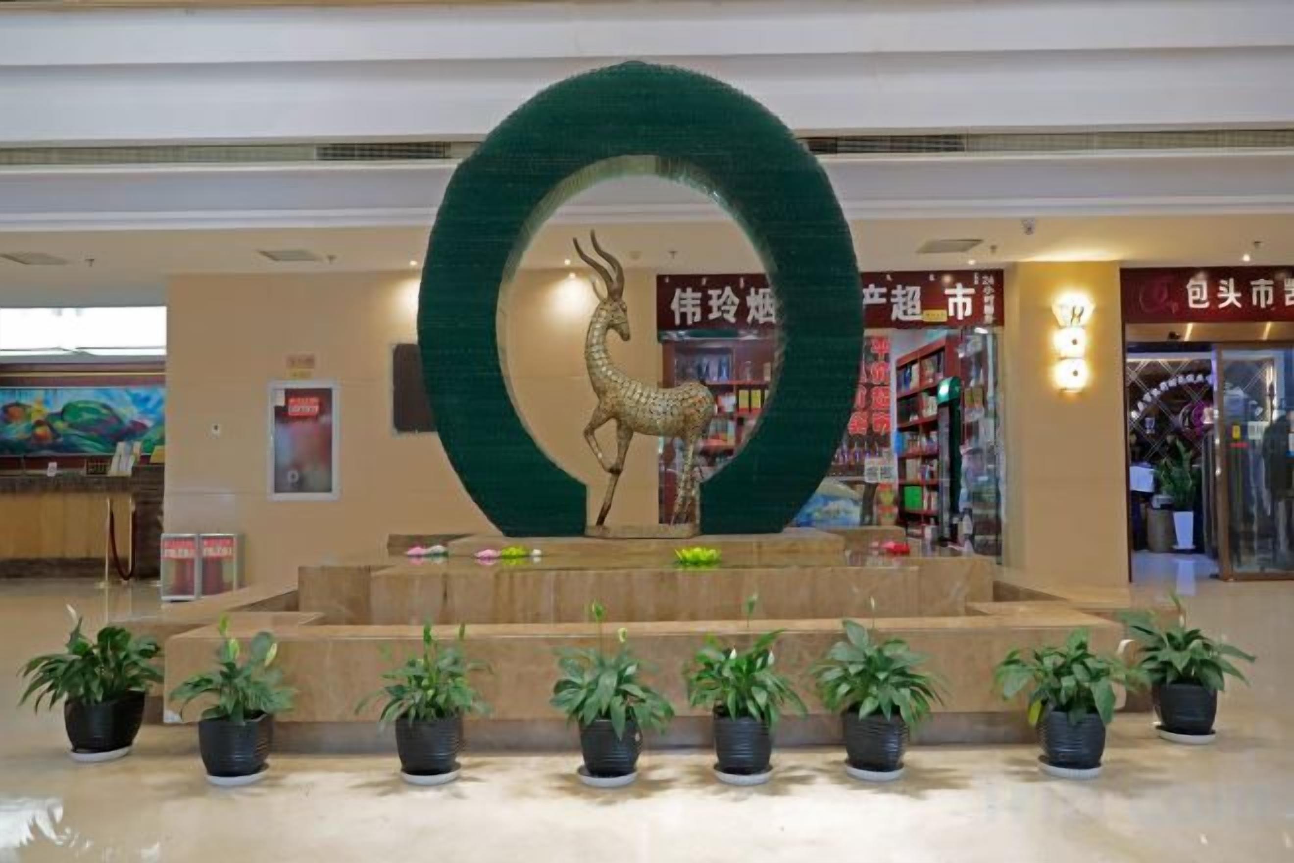 Een receptiezone met een grote ronde decoratie, een beeld en planten in potten.