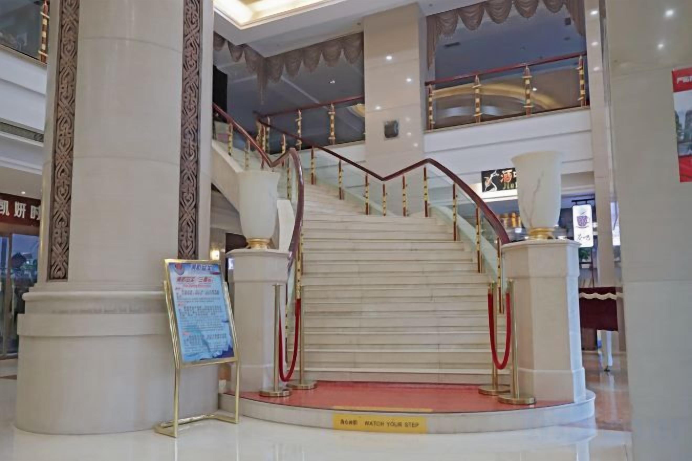 A grand staircase with a red carpet leading to an upper level, flanked by large white columns and a red railing.