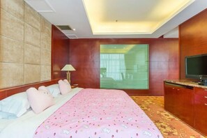 A bedroom with a bed, a TV, a window with blinds, and a wooden cabinet.