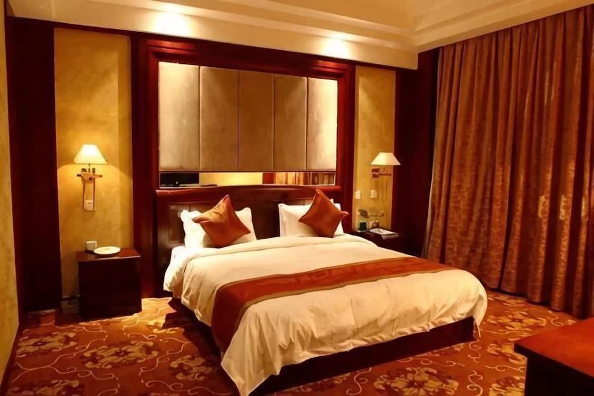 A hotel room with a large bed, two bedside tables, a nightstand, a mirror, and a curtain.