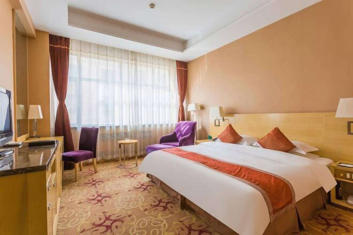 A hotel room with a large bed, a desk with a computer, a chair, a small table, and a TV.