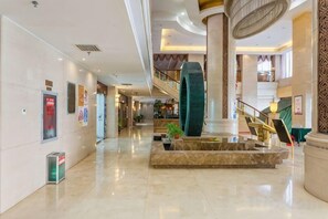 A spacious lobby with a central fountain, a staircase, and a large column. - Tianlong Hotel (Baotou)