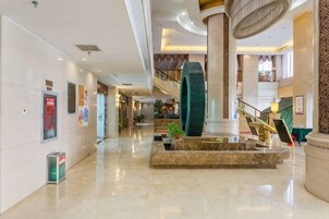 Um hall espaçoso com uma fonte central, uma escadaria e um grande pilar.