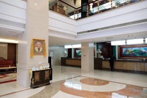 A spacious lobby with a high ceiling, a reception desk, and artwork on the walls. - Tianlong Hotel (Baotou)
