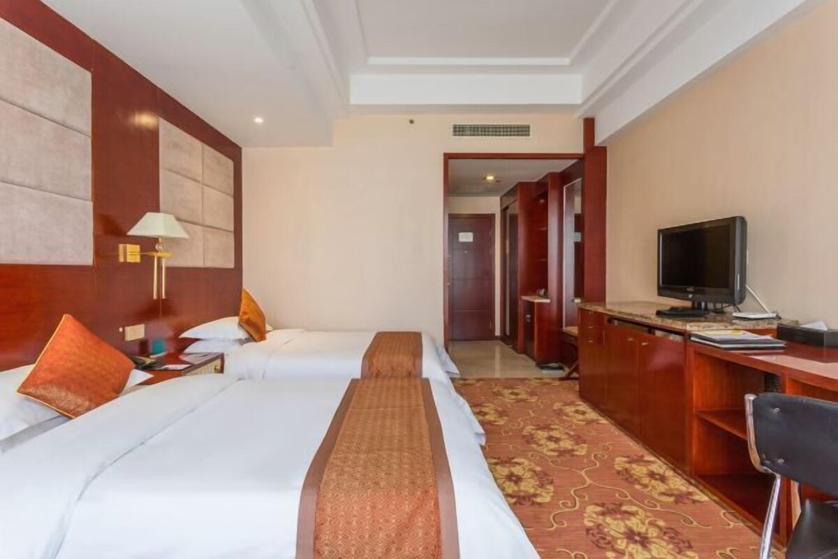 A hotel room with two beds, a desk, a television, and a carpeted floor.