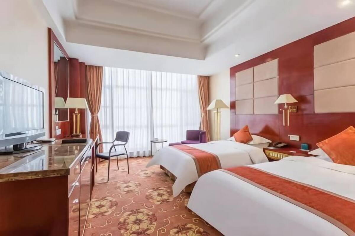 A hotel room with two beds, a desk with a television, a chair, and a window with curtains.