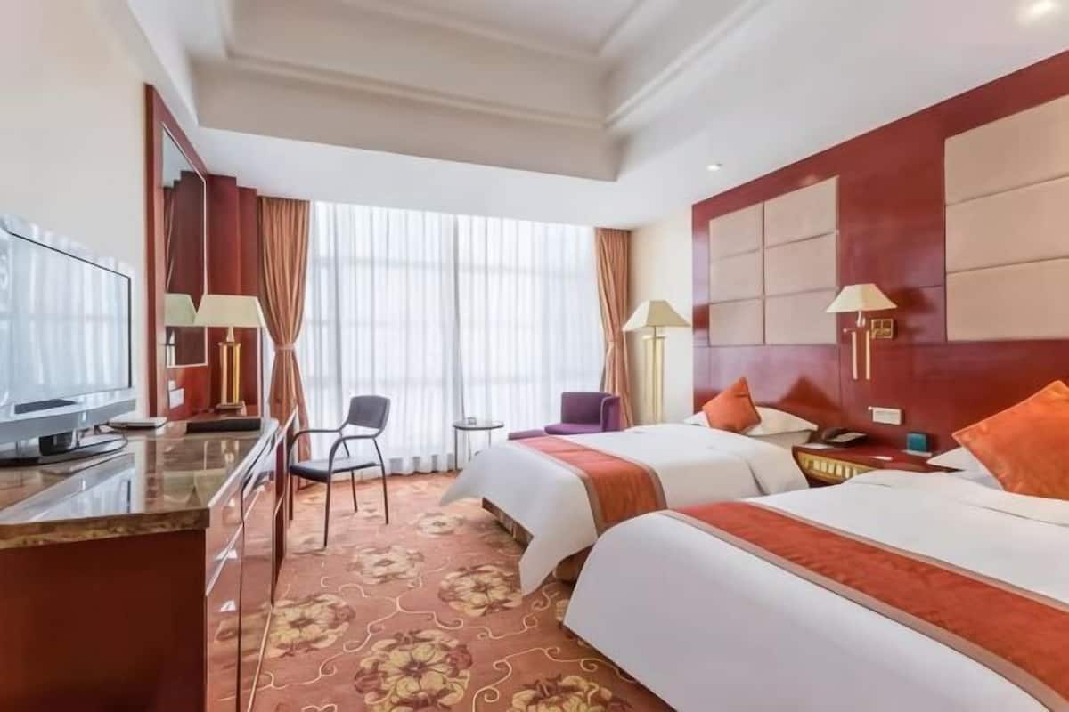 A hotel room with two beds, a desk with a television, a chair, and a window with curtains.