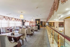 A hotel dining area with tables and chairs, a glass railing, and a view of the interior. - Tianlong Hotel (Baotou)