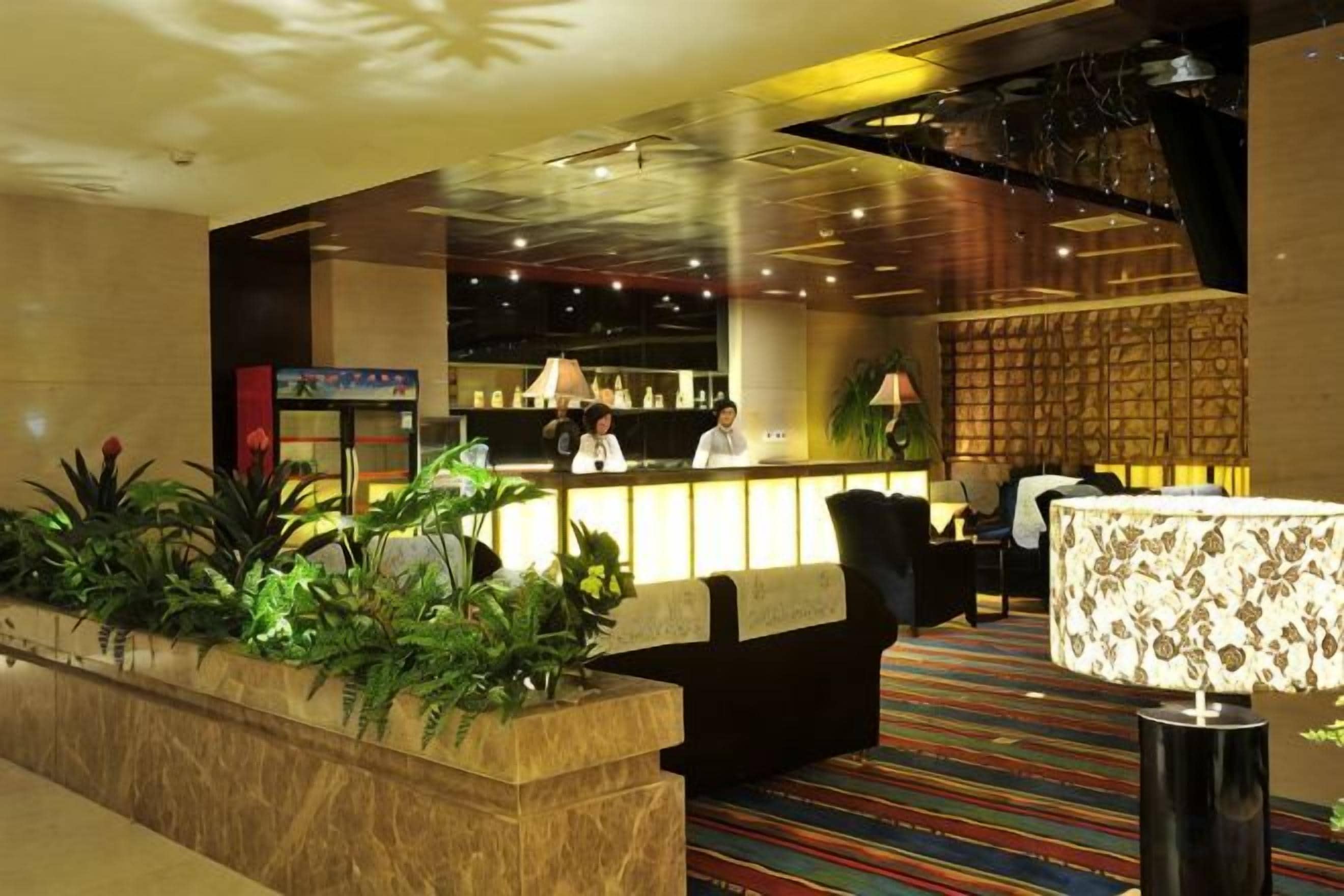 Un vestíbulo de hotel con mostrador de recepción, zona de estar y arreglos de plantas.