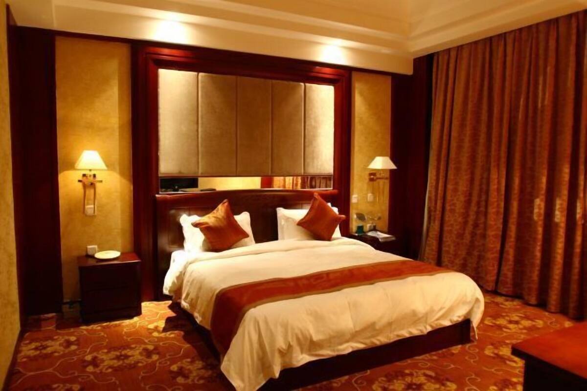 A hotel room with a large bed, two bedside tables, a nightstand, a headboard, and a curtain.