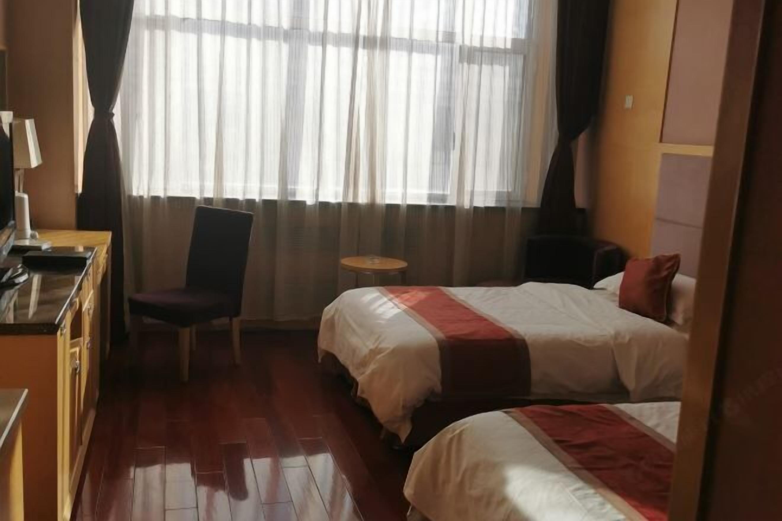 A hotel room with two beds, a desk, a chair, and a small table.