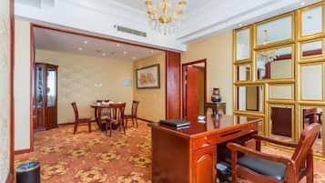 Ein Hotelzimmer mit Schreibtisch aus Holz, Stühlen, einer Deckenleuchte, einem großen Spiegel und Teppichboden.