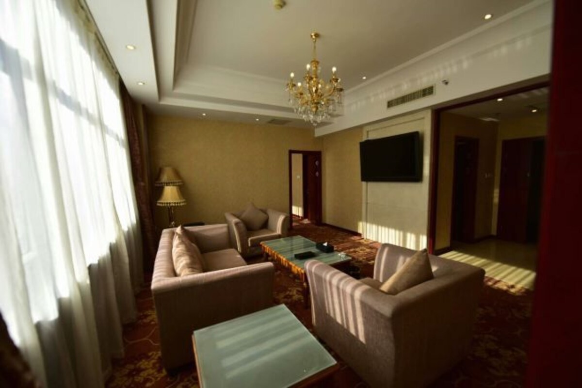 Quarto de hotel com sofá, mesa de centro, luminária e televisão.