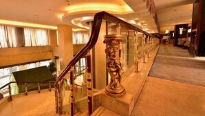 A grand staircase with ornate railings, a glass balustrade, and a view of a cityscape through large windows. - Tianlong Hotel (Baotou)