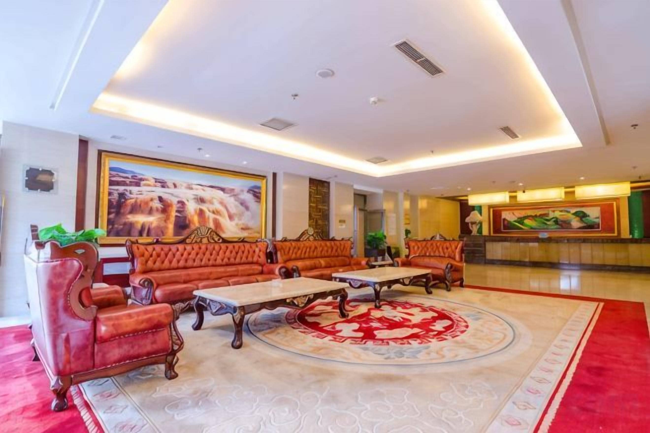 A hotel lobby with a red carpet, sofas, a coffee table, and a reception desk.