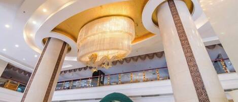 Un centro comercial de varios niveles con una gran lámpara de araña, columnas decorativas y un elemento arquitectónico circular.