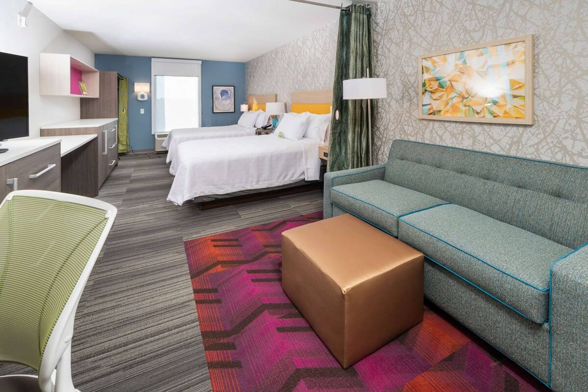 Une chambre d’hôtel avec deux lits, un canapé, un bureau, une chaise et un tapis à motifs.