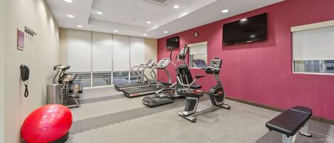 A fitness room with treadmills, elliptical machines, a red exercise ball, and a bench.