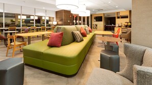 Een moderne zithoek met een groene bank, houten tafels en comfortabele zitplaatsen.