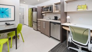 Een moderne keuken met een magnetron, koelkast en gootsteen. Er is een eettafel met stoelen en een bureau met een stoel.