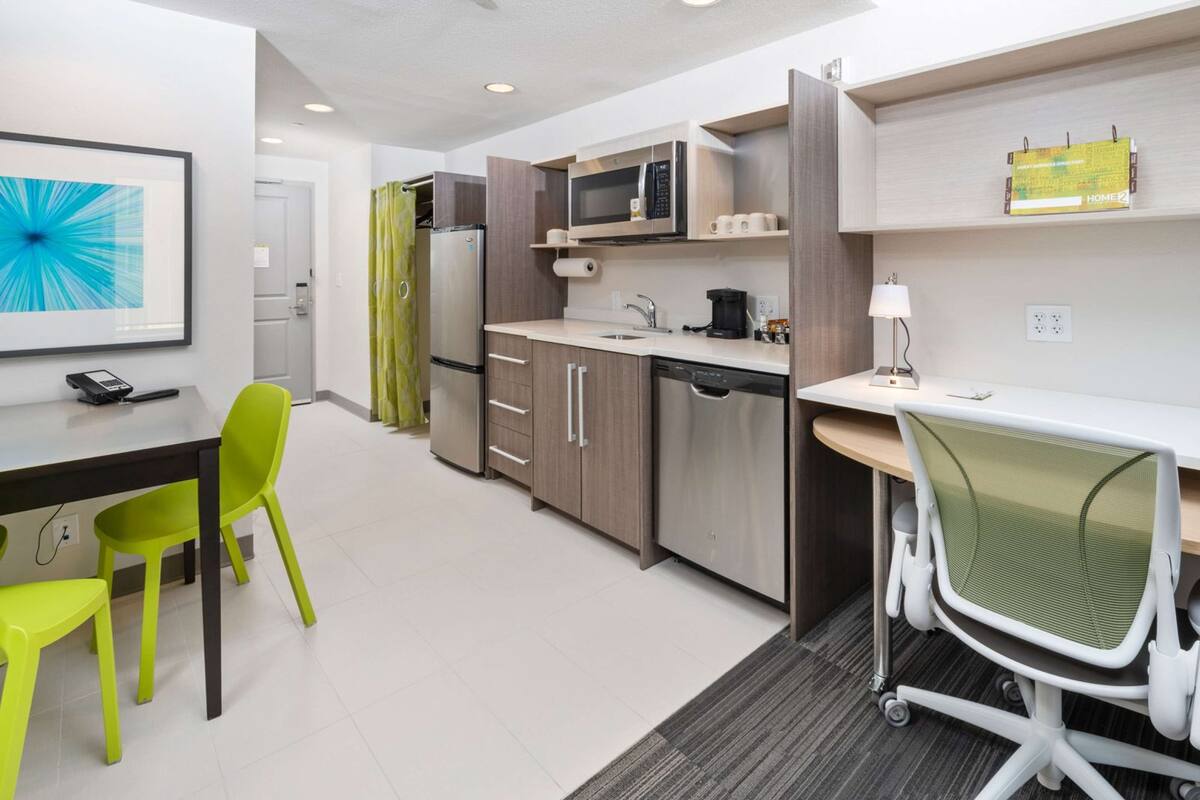 Une cuisine moderne équipée d’un four à micro-ondes, d’un réfrigérateur et d’un évier. On y trouve une table à manger avec des chaises, ainsi qu’un bureau avec une chaise.