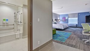 A hotel room with a shower, a bed, a desk, and a chair. - Home2 Suites by Hilton Springdale (Springdale)
