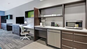 A modern kitchen with a built-in microwave, coffee maker, and a sink. There is a desk with a computer and a chair. - Home2 Suites by Hilton Springdale (Springdale)