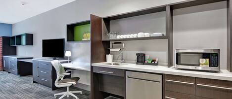 A modern kitchen with a built-in microwave, coffee maker, and a sink. There is a desk with a computer and a chair.