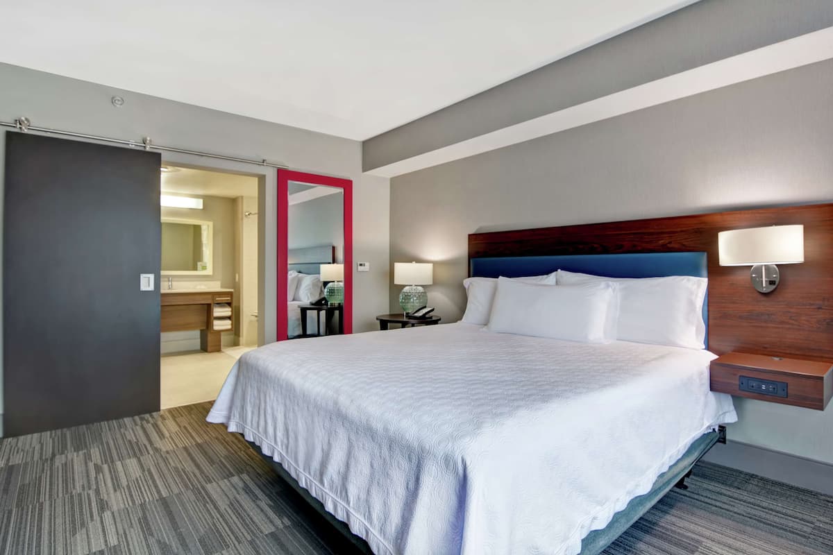 Ein Hotelzimmer mit einem großen Bett, einem hölzernen Kopfteil, einem Nachttisch mit Lampe und einem Spiegel.