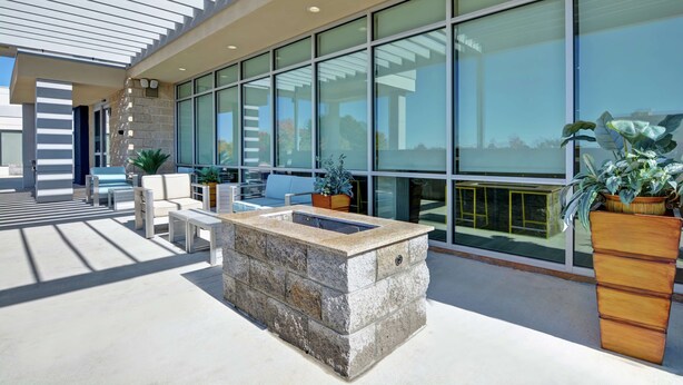 A modern outdoor seating area with stone planters and a fire feature, large windows, and a clear view of the sky. - Home2 Suites by Hilton Springdale (Springdale)