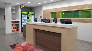 A hotel reception area with a counter, a self-service kiosk, a refrigerator with cold and really cold sections, and a shelf with snacks. - Home2 Suites by Hilton Denver South/Centennial Airport (Centennial)