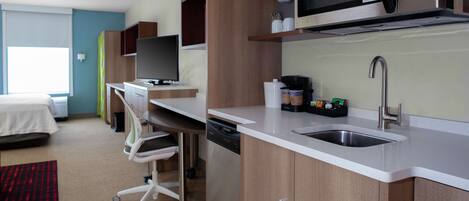 A compact hotel room with a kitchenette, a bed, a desk, and a television.