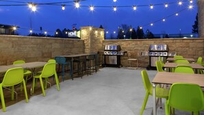 An outdoor patio with tables and chairs, string lights, and a stone wall. - Home2 Suites by Hilton Denver South/Centennial Airport (Centennial)