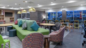 A modern lounge area with a green sofa, colorful patterned chairs, and a large flat-screen TV. - Home2 Suites by Hilton Denver South/Centennial Airport (Centennial)