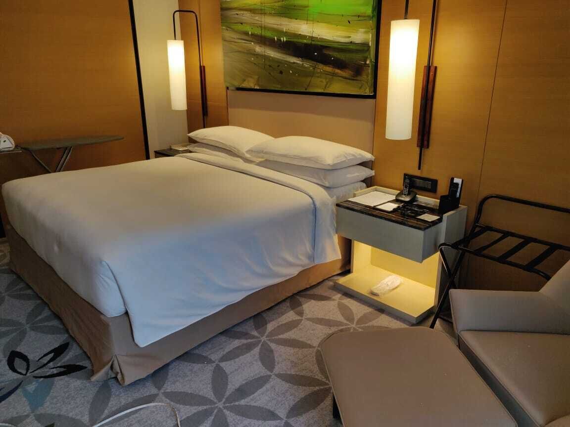 A hotel room with a bed, bedside table, lamp, and a painting on the wall.