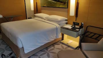 A hotel room with a bed, bedside table, lamp, and a painting on the wall.