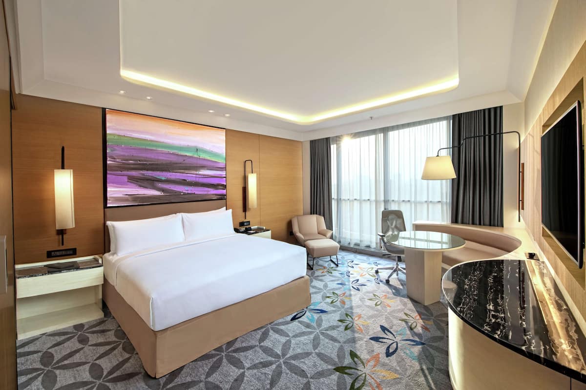 Une chambre d’hôtel avec un grand lit, un bureau, une chaise, une télévision et un tableau au mur.