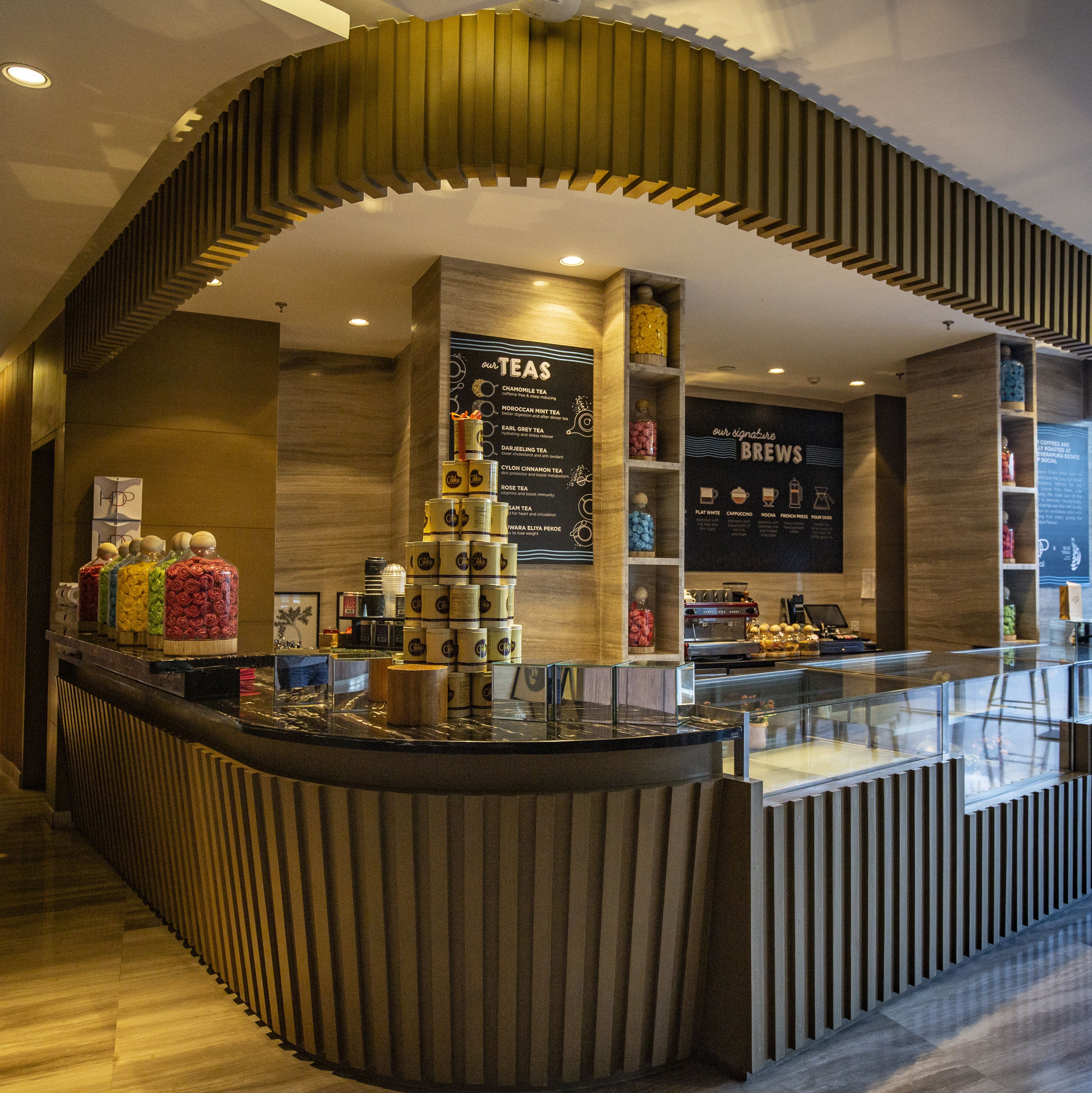 A modern coffee shop with a curved counter, a menu board, and various coffee containers.