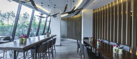 A modern dining area with long tables, chairs, and a view of greenery outside.