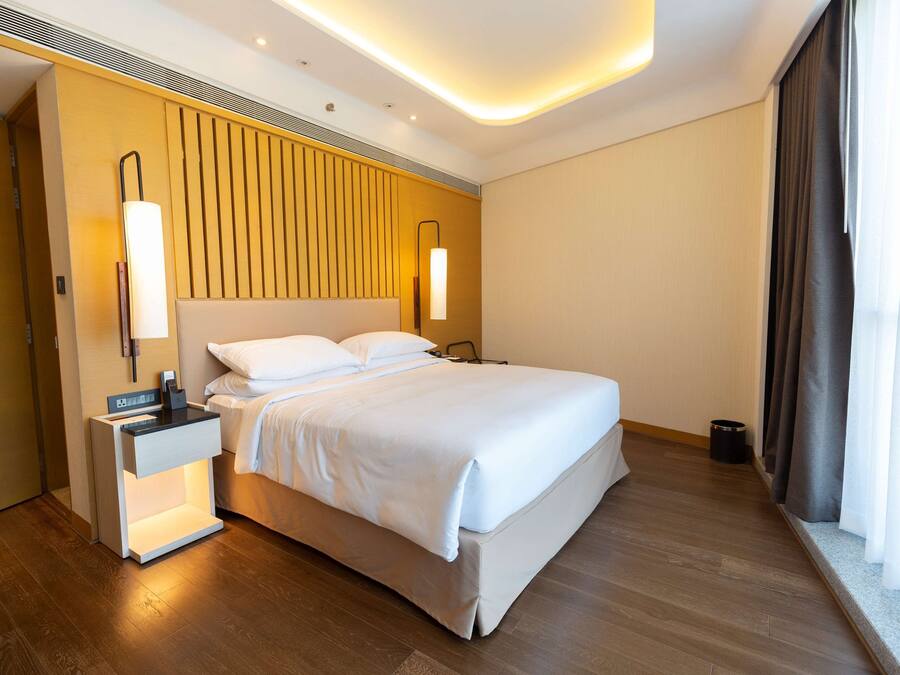 Une chambre d’hôtel moderne avec un grand lit, des lampes de chevet, une table de nuit et un mur revêtu de panneaux en bois.