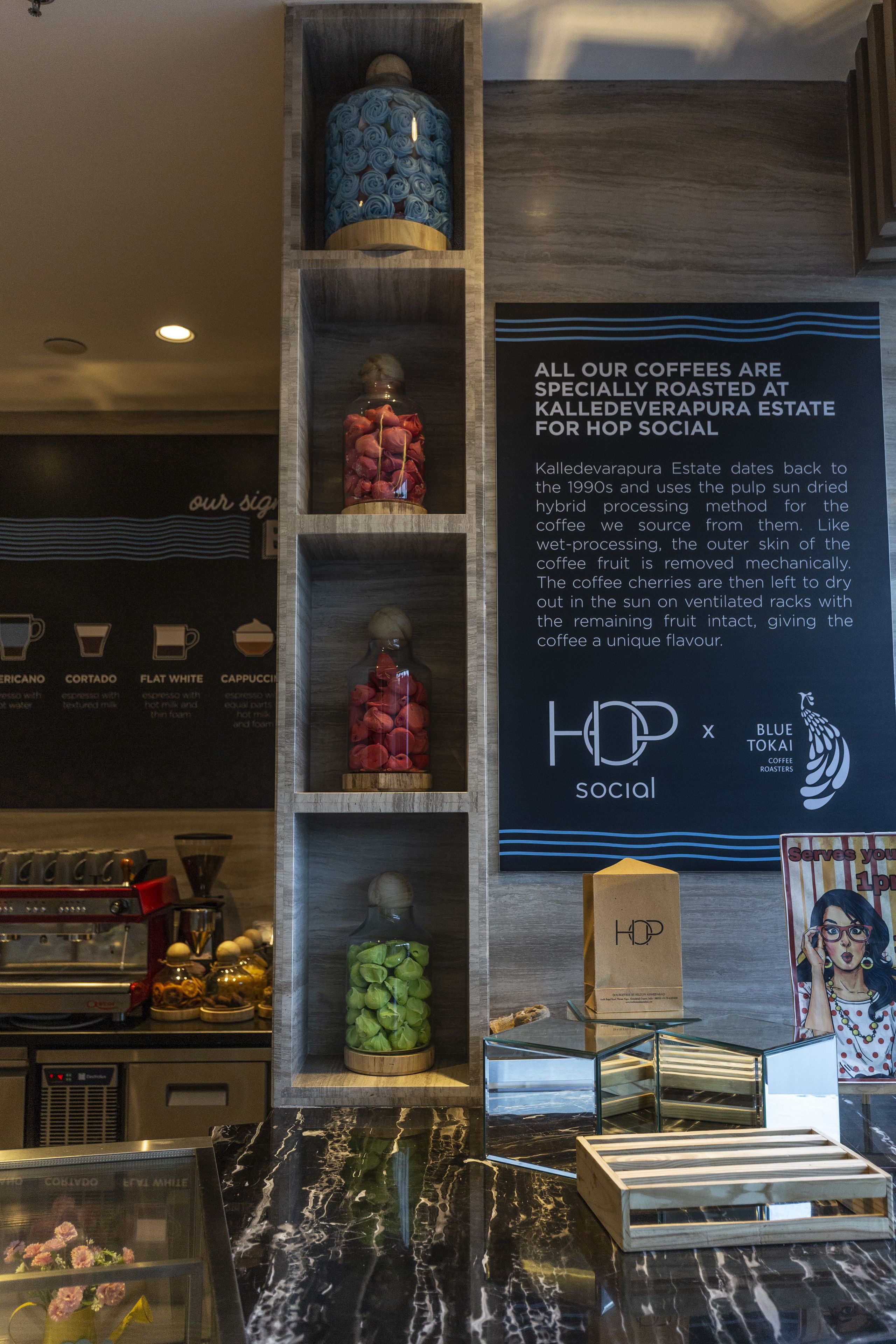 Interior de una cafetería con un cartel sobre tostado de café, una exhibición de granos de café y una máquina de café.
