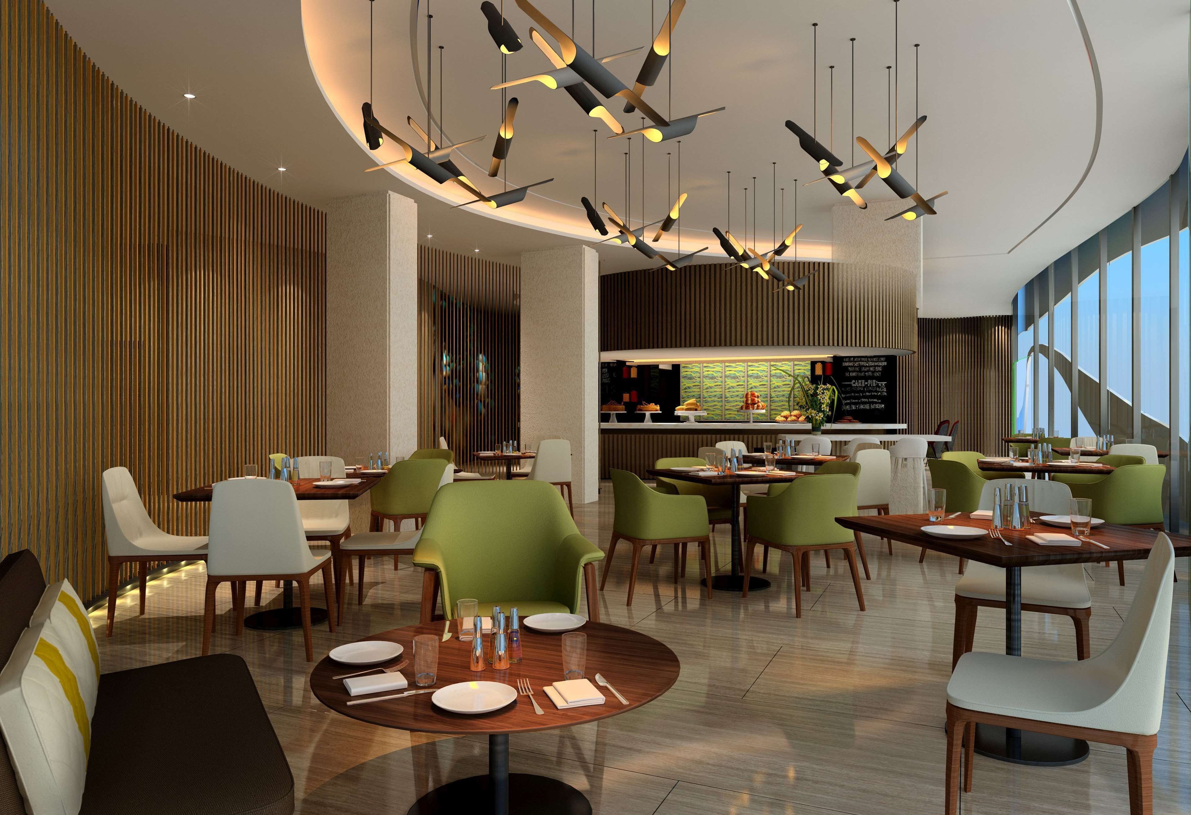 A modern restaurant with round tables, green chairs, and unique ceiling lights.