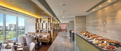 A modern dining area with a buffet, wooden flooring, and large windows offering a city view.