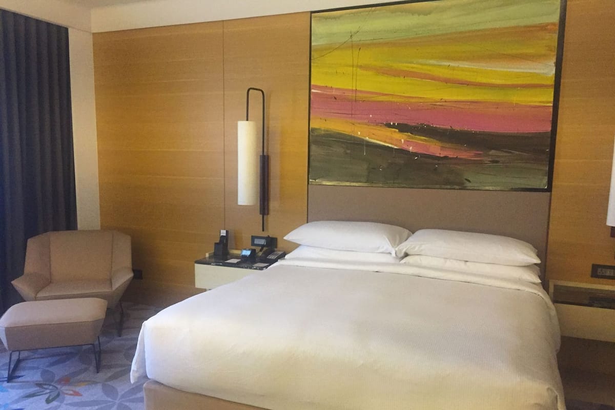 Une chambre d’hôtel avec un lit, une chaise, une table de chevet, un téléphone et un tableau au mur.